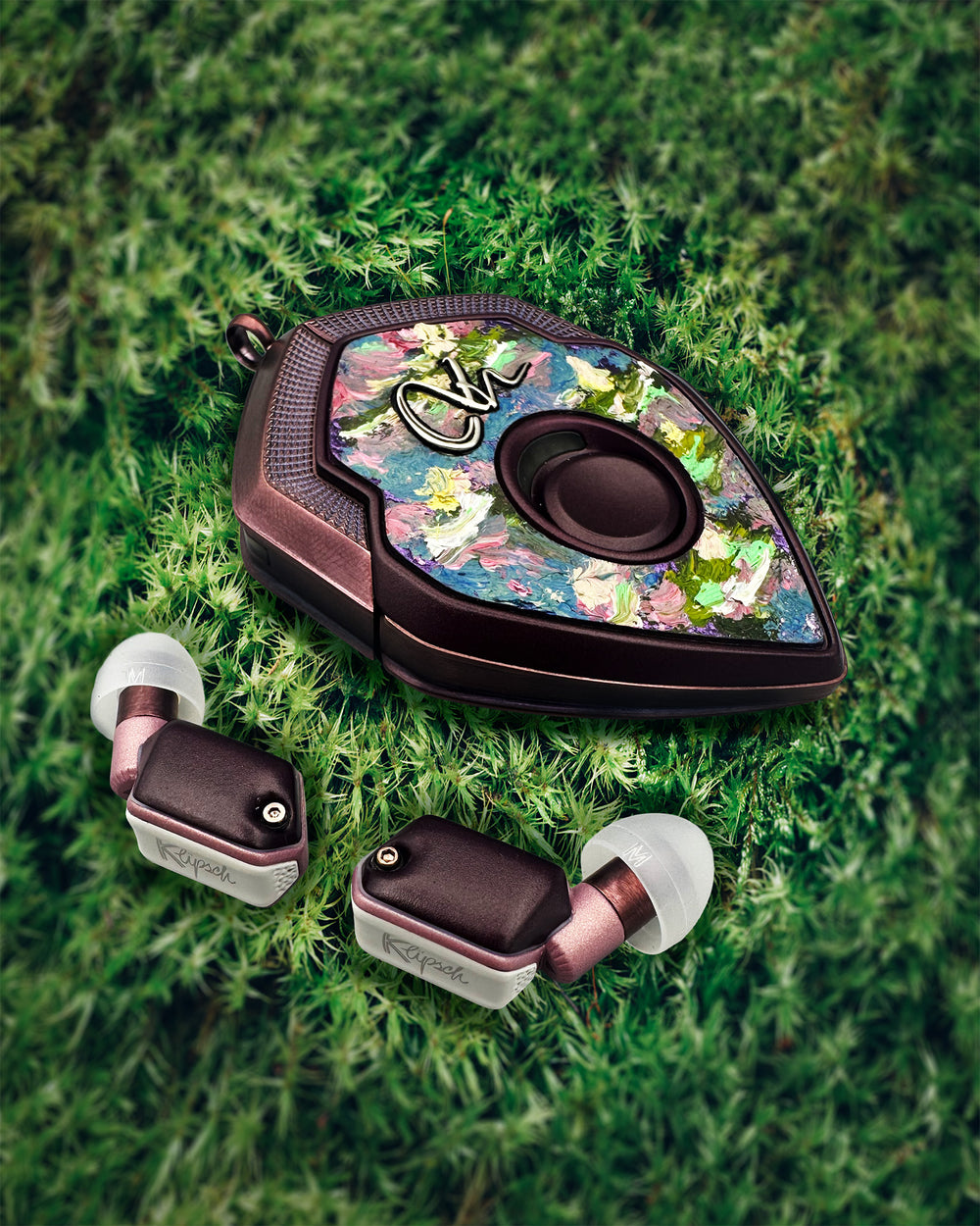 Ahonoukoun Deux charging case with hand-painted leather cover and bronze earbuds on moss