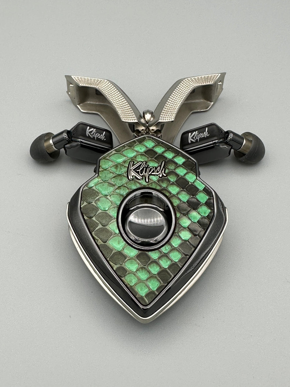 Green Machine charging case with knurled nickel doors open and black earbuds tucked beside it