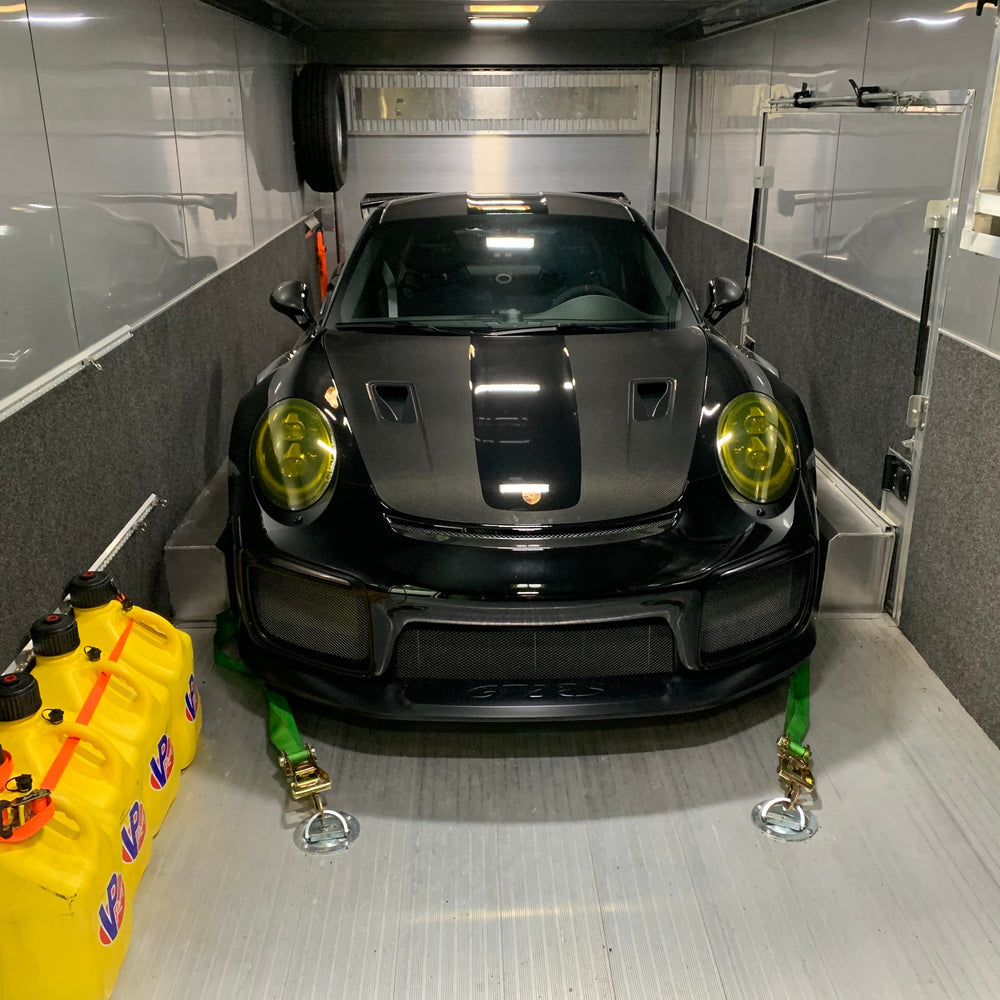 Black Porsche 911 GT2 RS with yellow-tinted headlights strapped down in an enclosed trailer
