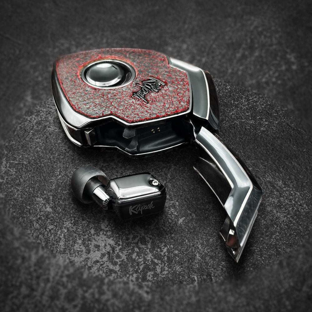Oxblood case open with chrome door and a black earbud on dark stone