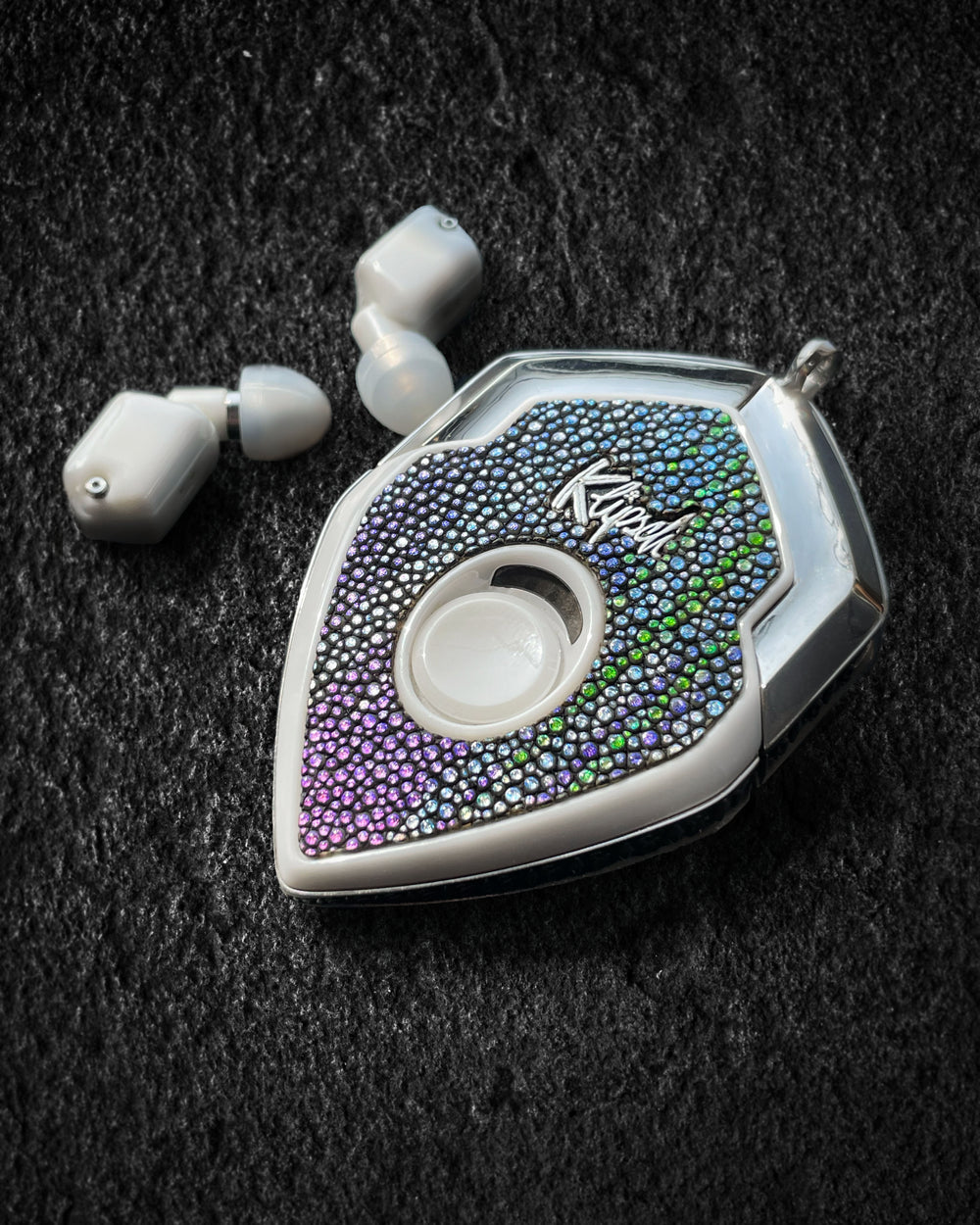 Stingray Filigree charging case with iridescent stingray face and white earbuds on black fabric